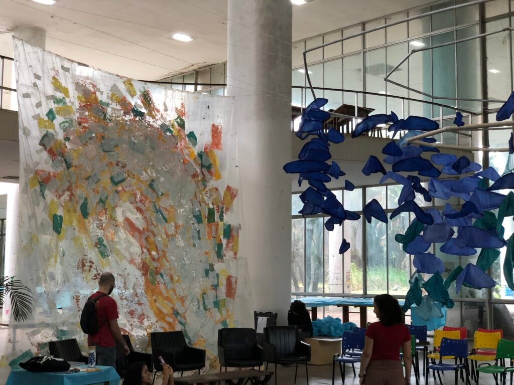 Interior gallery view showcasing hanging white lace installations and abstract blue sculptures, by Osmar