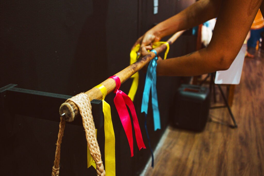 Close-up photo of hands organizing colorful ribbons hanging from a wooden rack, scenography by Osmar