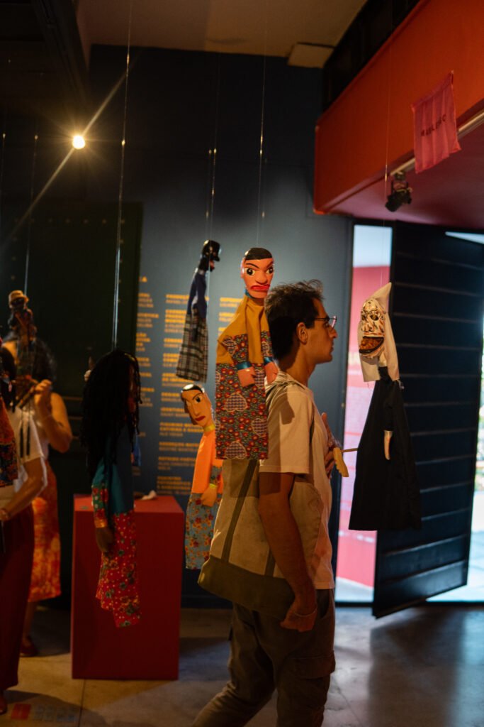 Gallery snapshot capturing visitors admiring traditional vibrant costumes displayed on mannequins, curated by Osmar