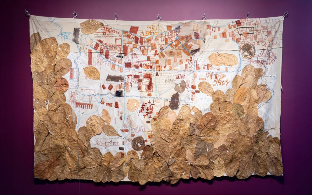Complete view of a framed horizontal collage art piece mapping urban territories using fabric textures, by Osmar