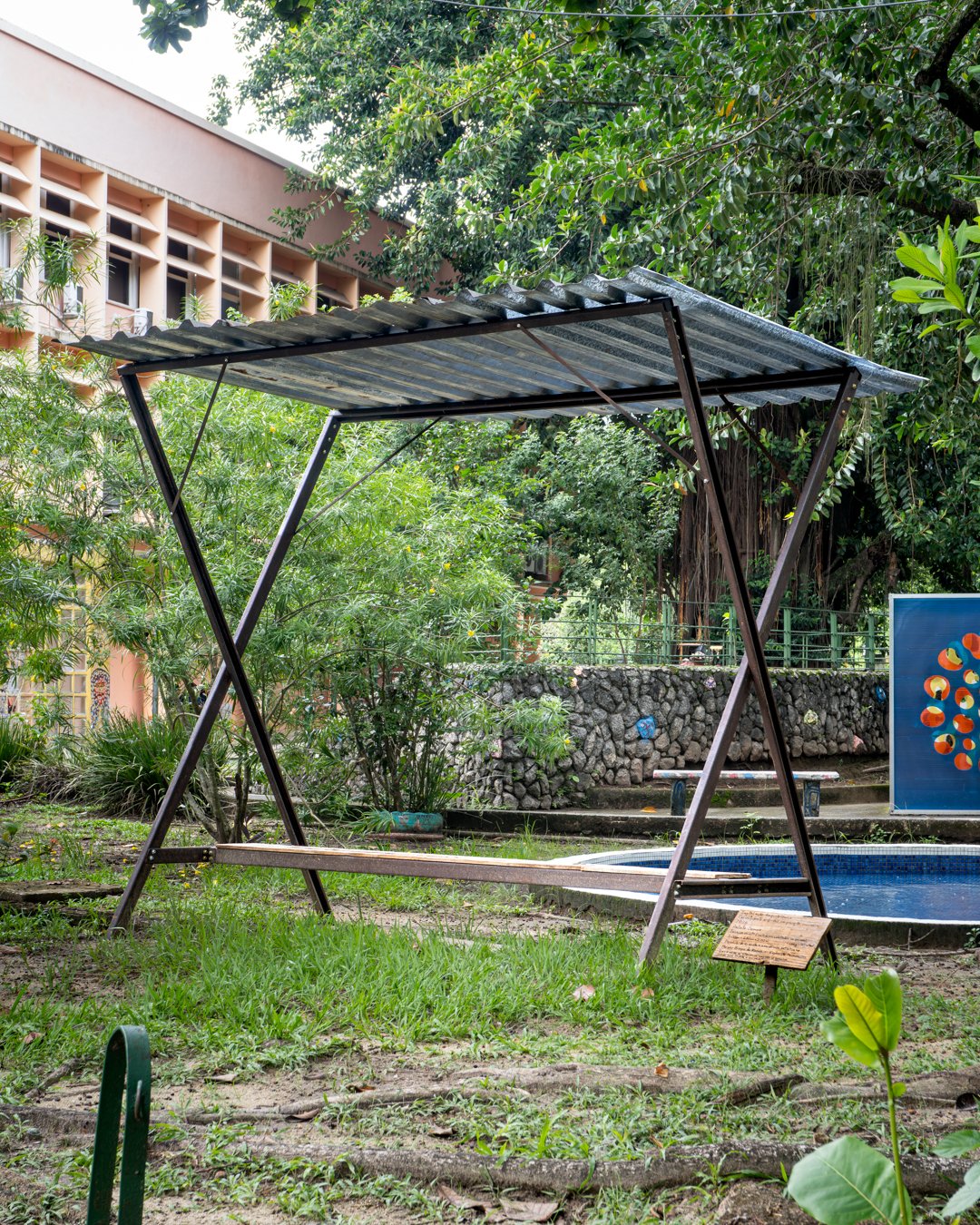 Dark metallic canopy installation sitting on a lawn area next to lush trees, designed by Osmar