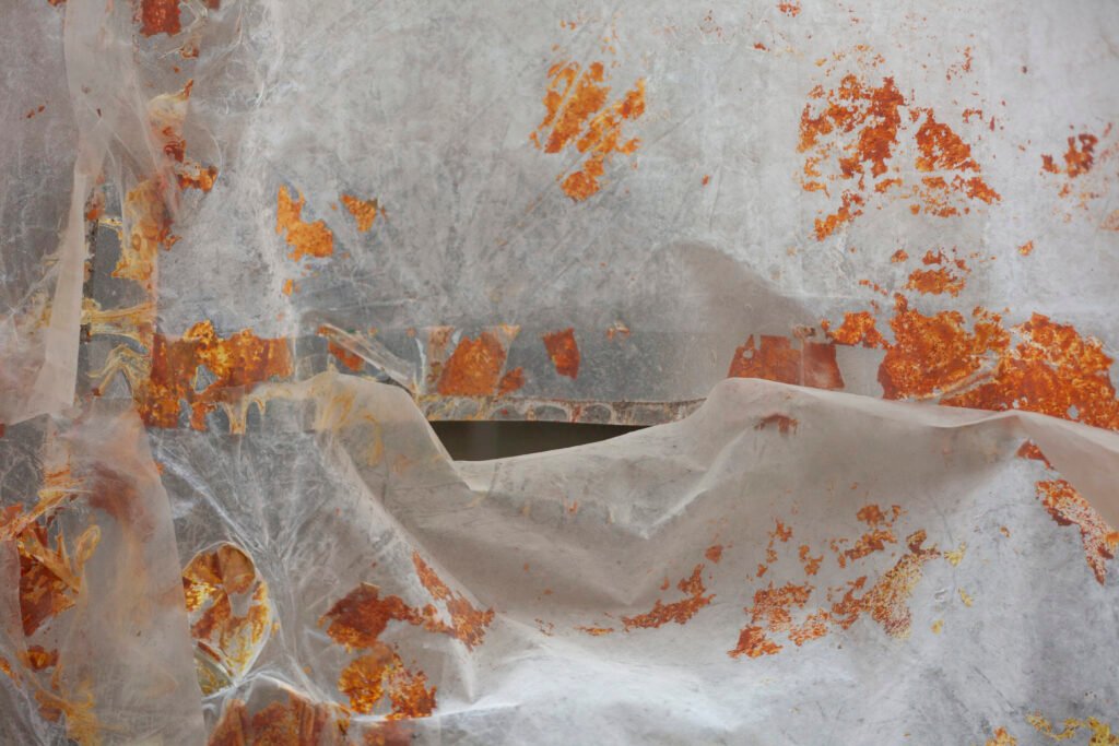 Delicate white translucent fabric sheet detailed with faint orange paint markings hanging indoors, by Osmar