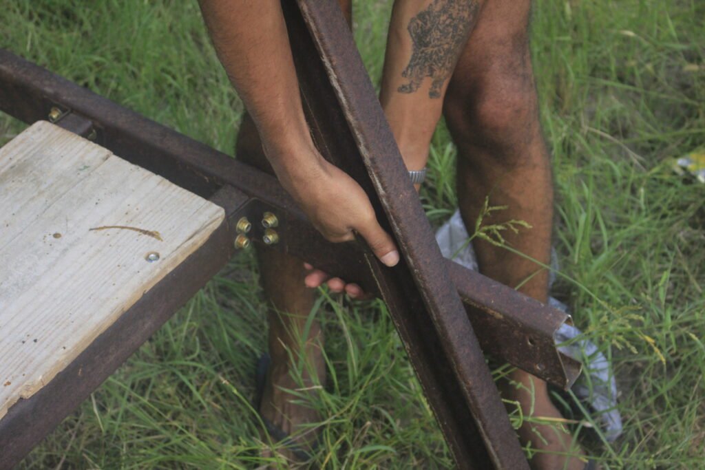 Close-up of hands checking the structural joints of an overlapping dark timber post arrangement, by Osmar