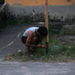 Outdoor shot showing a person leaning down to adjust equipment near a graffiti wall, sound art by Osmar