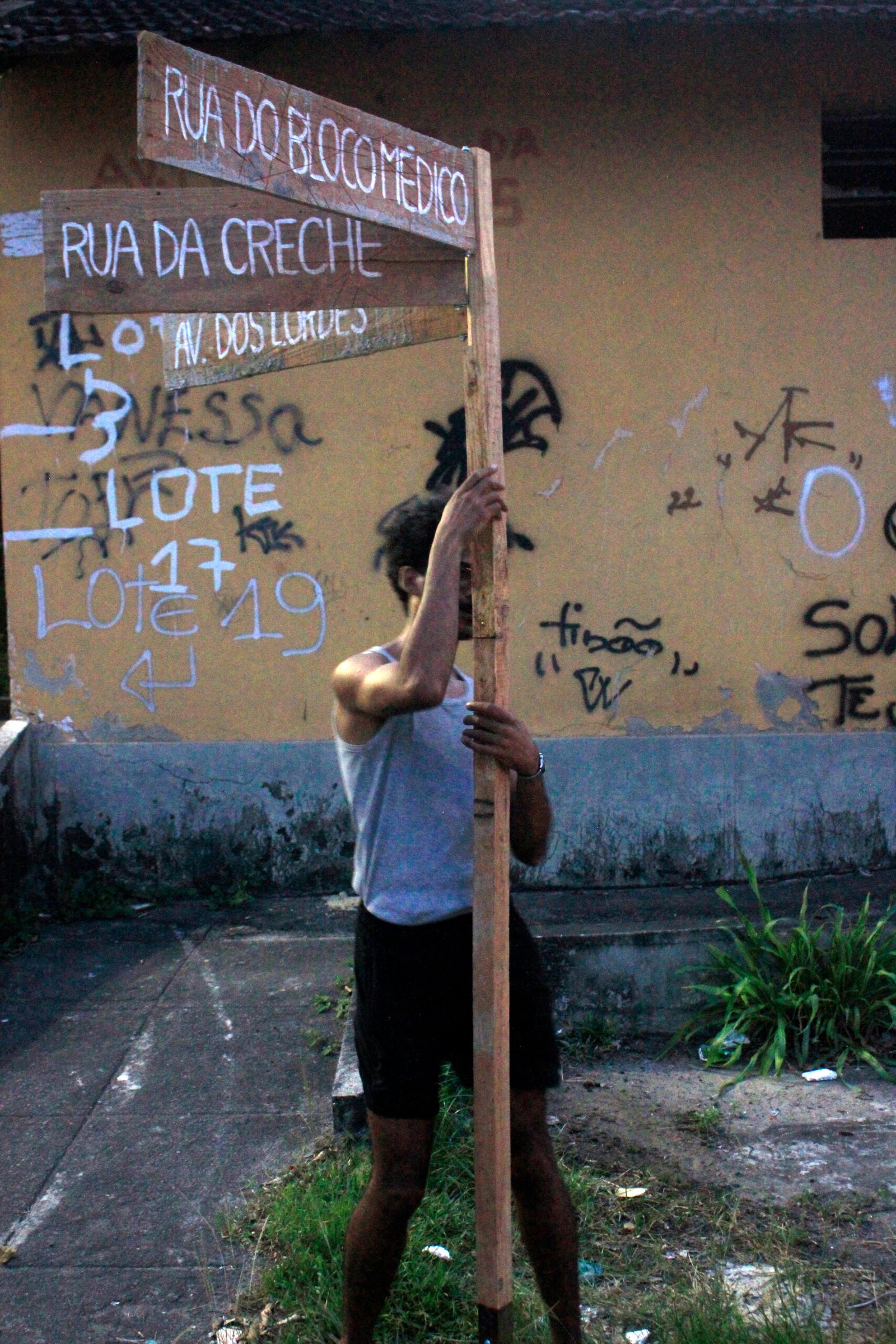 Back view of a young man holding a wooden slat against a yellow graffiti wall, art performance by Osmar