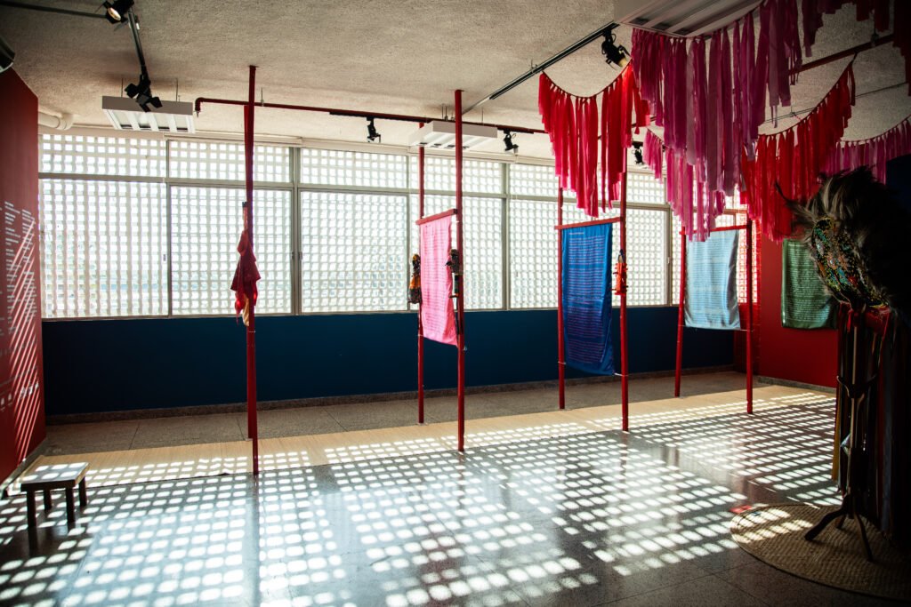 Interior space showing a series of windows flanked by hanging decorative pink fabric layers, by Osmar